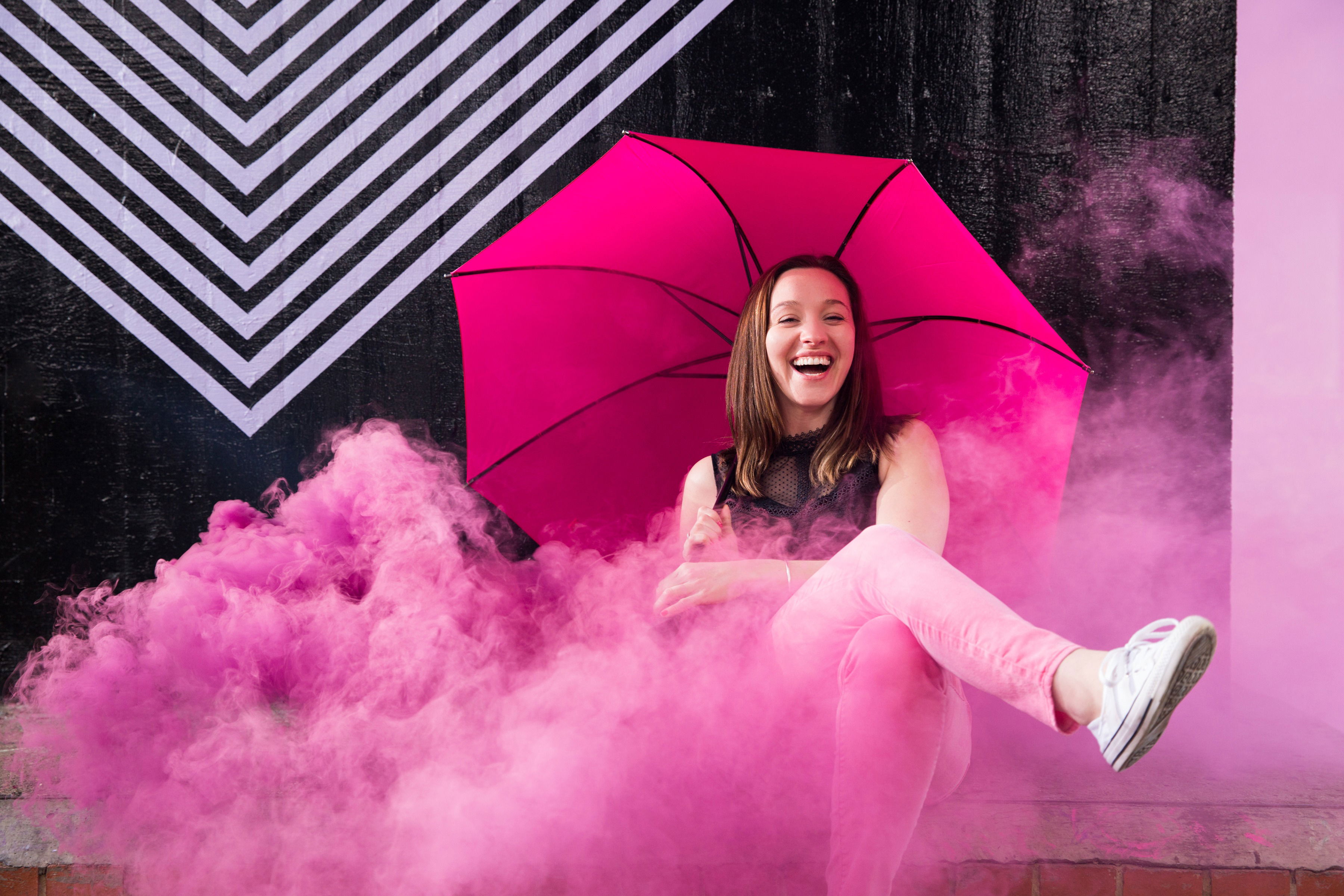 Cordelia laughing under a pink umbrella in a cloud of pink smoke